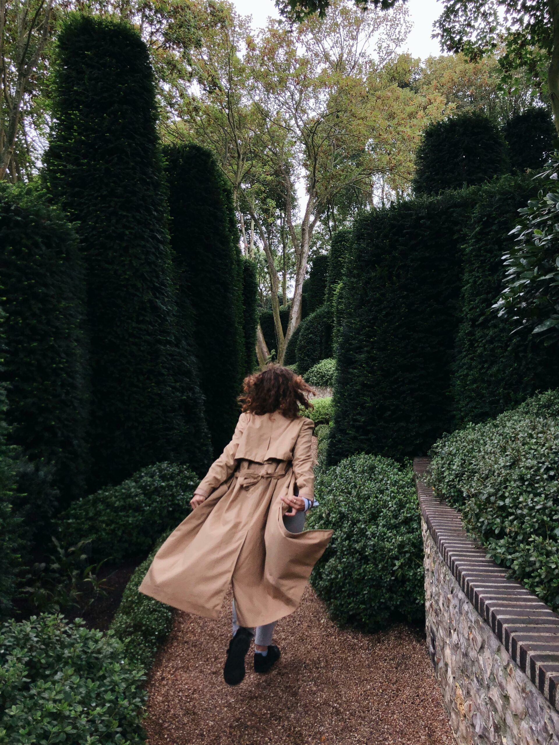 Une femme qui court dans une allée avec des arbres taillés